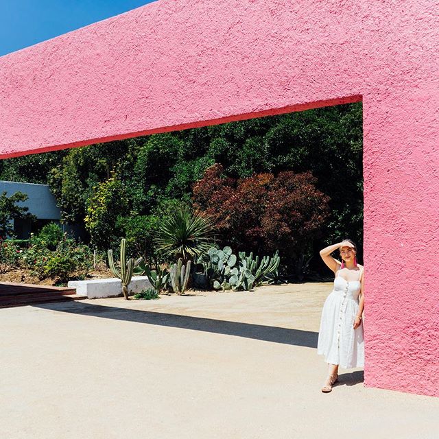 This is a photo of a girl standing under a large pink block-like architectural structure.